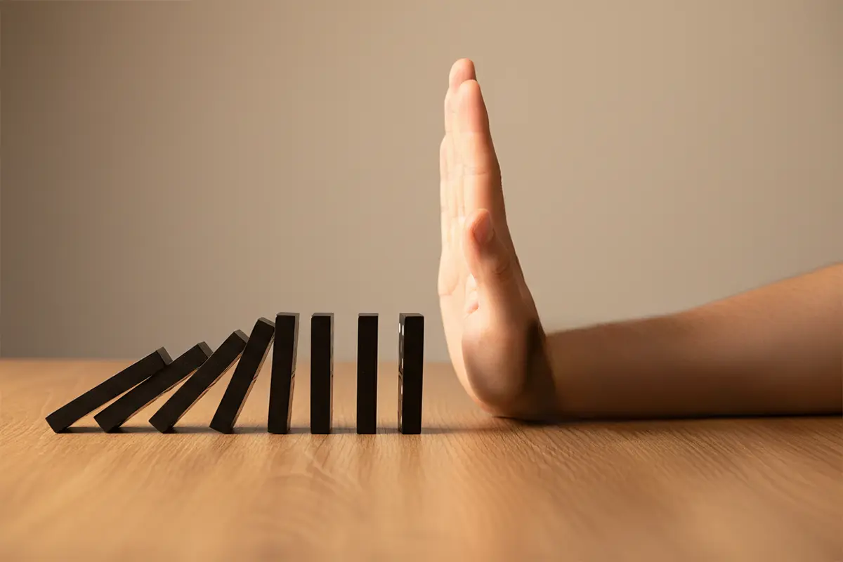 Hand stoppt symbolisch fallende Dominosteine – Symbolbild für verantwortungsvolles Wetten